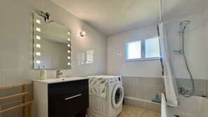 Ein modernes Badezimmer mit Waschbecken, Spiegel, Waschmaschine und Dusche.