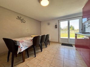 Zona pranzo con tavolo ricoperto da una tovaglia fantasia, quattro sedie, orologio a parete e una porta che dà sull'esterno.