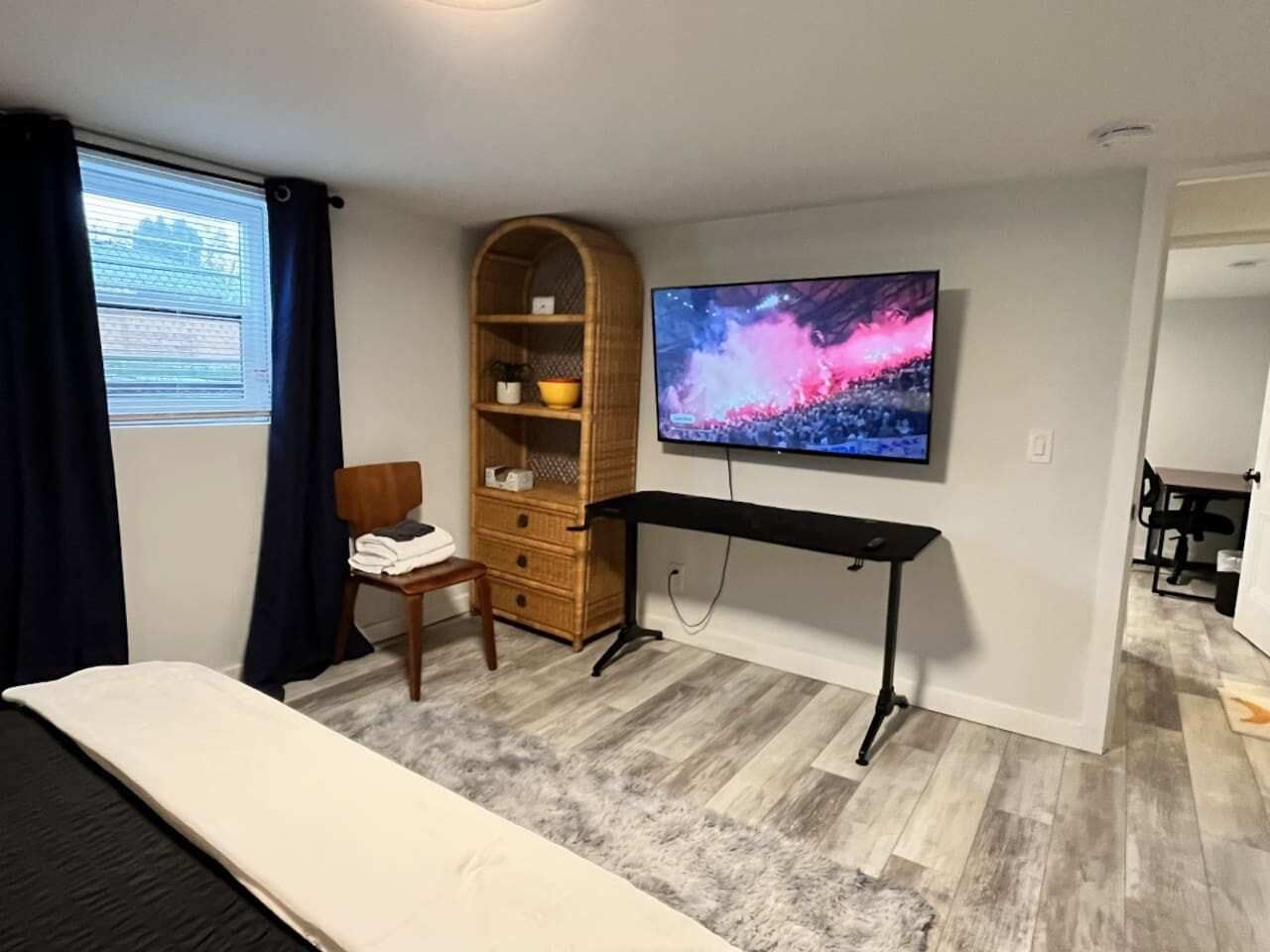 Een slaapkamer met een bed, een aan de muur bevestigde televisie, een houten stoel, een bureau en een kledingkast.