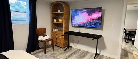 Een slaapkamer met een bed, een aan de muur bevestigde televisie, een houten stoel, een bureau en een kledingkast.