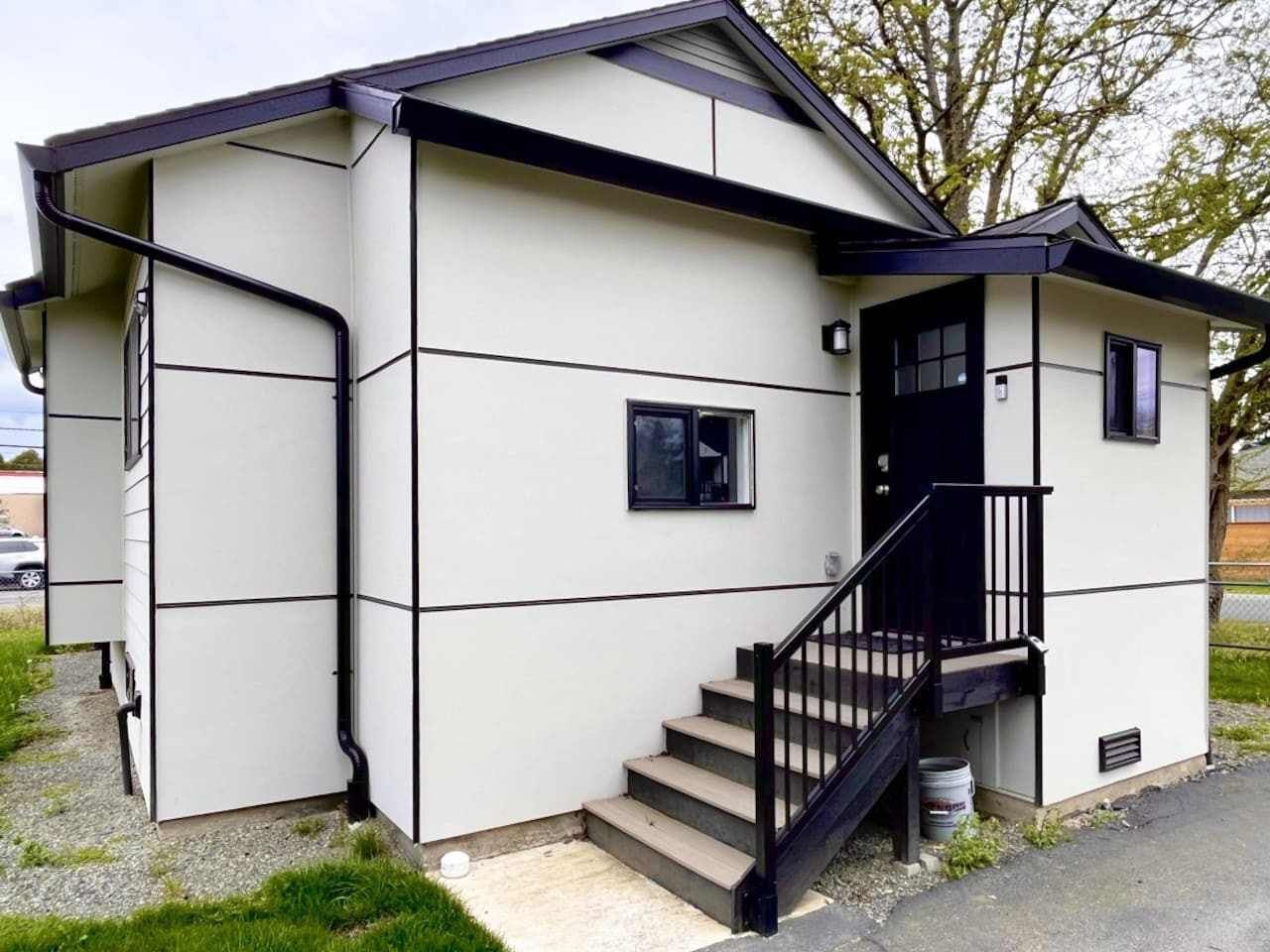 A small, single-story building with a staircase leading to a door, a small window, and a visible garage door.