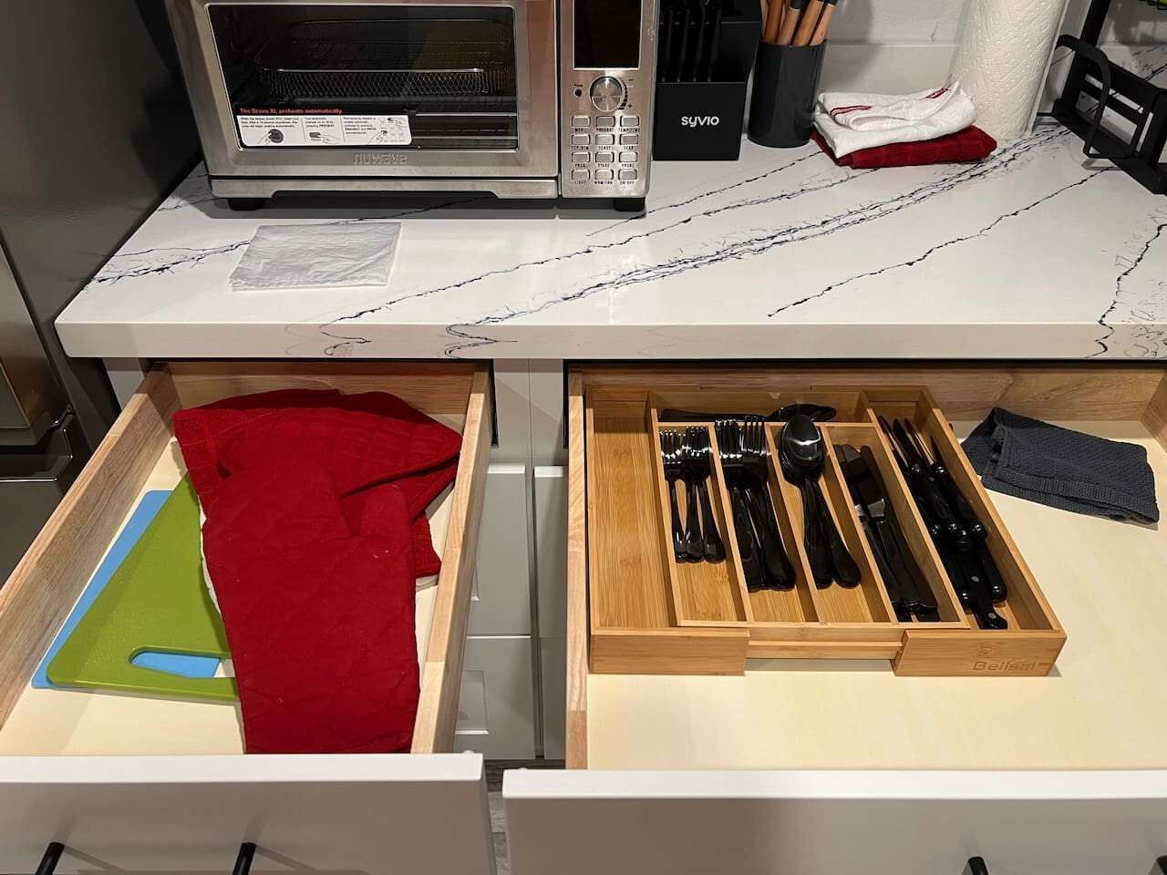 A kitchen with a microwave, a drawer with utensils, and a red cloth.