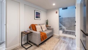Una sala de estar moderna con un sofá gris, una mesita auxiliar, un cuadro enmarcado en la pared y una escalera que conduce a un balcón.