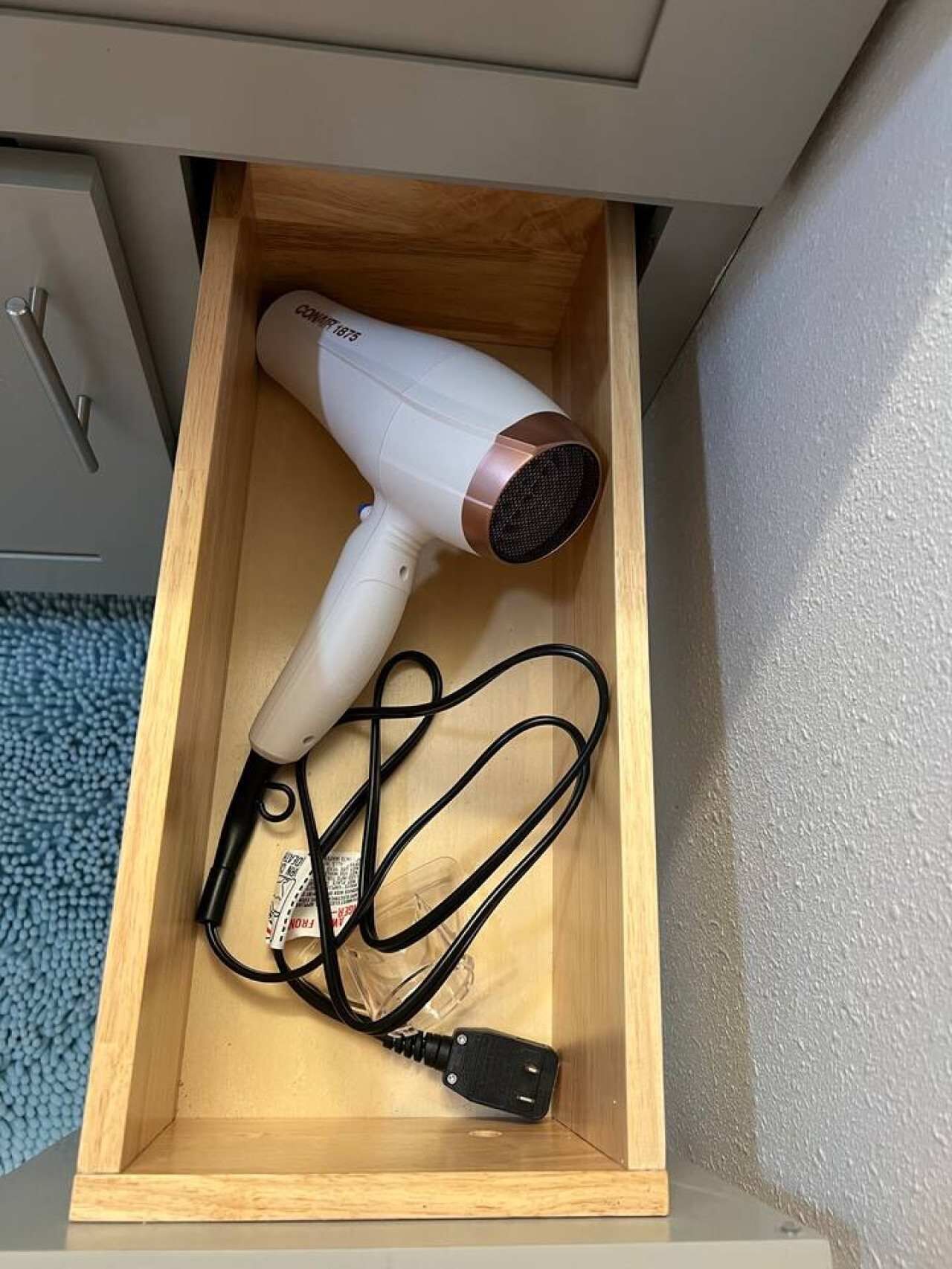 Un tiroir contenant un sèche-cheveux blanc avec un cordon noir et un adaptateur secteur.