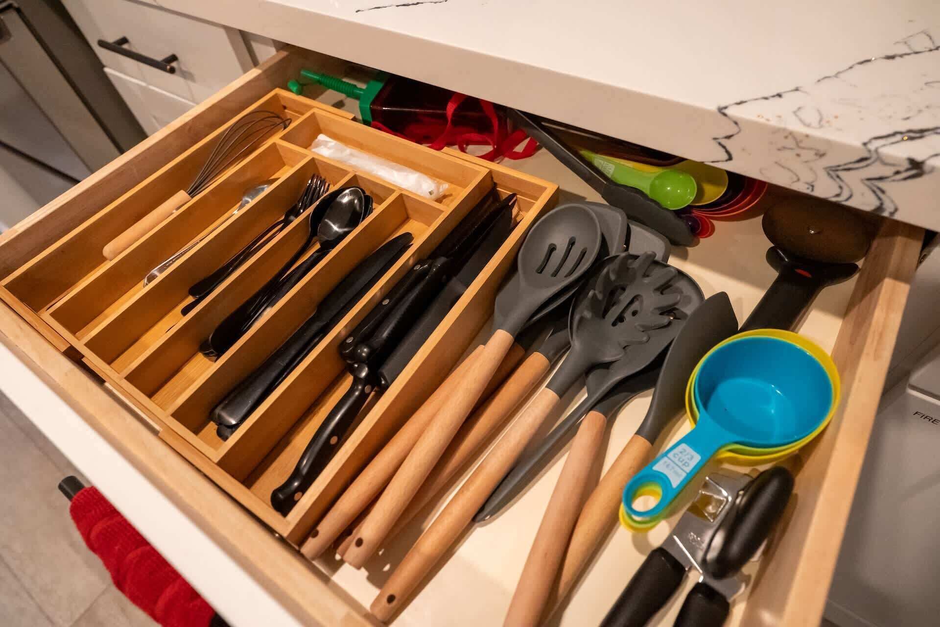 Een lade gevuld met verschillende keukengerei, waaronder messen, spatels en een maatbeker.