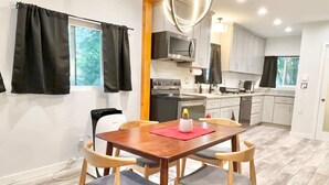 Een compacte keuken met moderne apparatuur, een eethoek met een houten tafel en stoelen, en uitzicht op de omgeving door een raam.