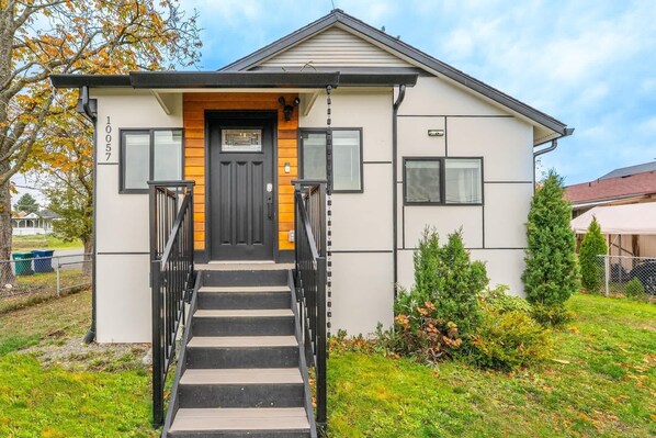 Une maison moderne à deux étages, avec une porte d’entrée noire, un escalier menant à l’entrée et un petit porche.