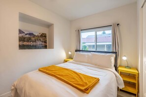 Une chambre à coucher avec un lit, un tableau, une fenêtre avec des rideaux et des lampes de chevet.