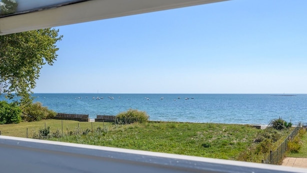 A view of the sea from a window overlooking a grassy area with a fence and a wooden structure. - Bright house 9 pers, beach access, parking, Sarzeau (Sarzeau)