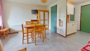 A compact living space with a dining area, kitchenette, and a television mounted on the wall.