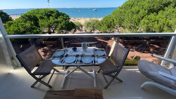 Un balcone con un tavolo apparecchiato per due, con vista su una spiaggia con barche e persone.