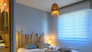 A bedroom with a bed, pillows, a bedside lamp, a hanging light fixture, and a window with blinds. - Holiday home 4 ppl - Sea view & beach access - Sarzeau (Sarzeau)