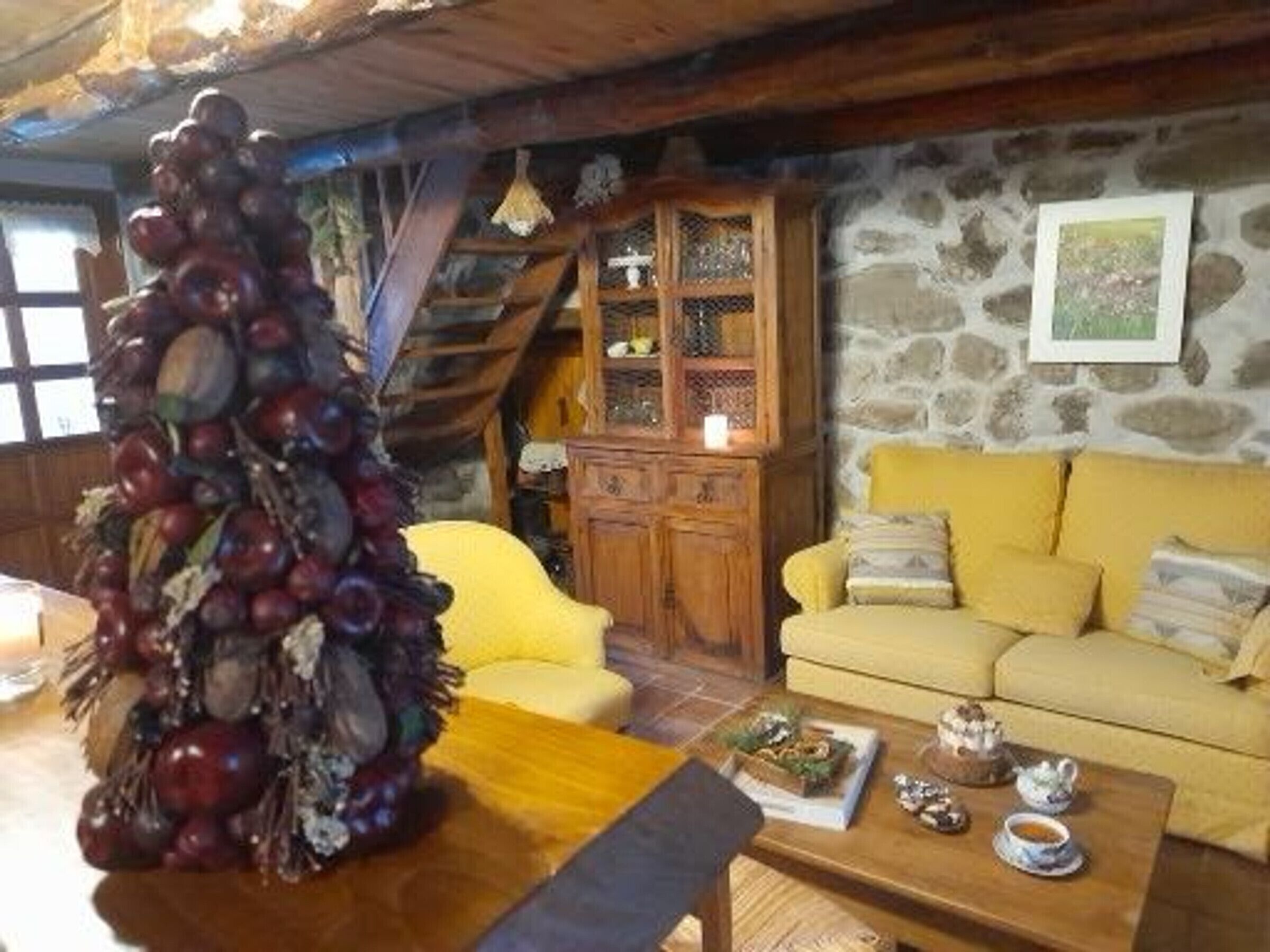 A cozy living room with a stone wall, a yellow sofa, a wooden cabinet, and a Christmas tree.