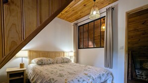 A bedroom with a wooden ceiling, a bed with floral bedding, a nightstand, a lamp, and a window with curtains. - Renovated cottage for 4 pers. with equine accommodation, Saint-Front (Saint-Front)