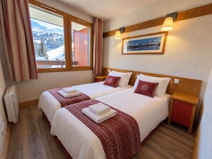 A hotel room with two beds, a window with curtains, a framed picture on the wall, and a small bedside table. - Bright apartment near slopes, pool access, pets allowed (La Plagne 1800)