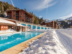 A pool area with wooden buildings and snow-covered surroundings. - Bright apartment near slopes, pool access, pets allowed (La Plagne 1800)