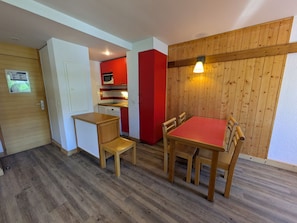 A compact kitchen with red cabinets, a microwave, and a dishwasher. There is a dining area with a red table and wooden chairs.