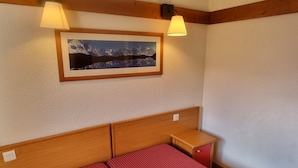 A room with a wooden headboard, a bed with red striped bedding, a nightstand, a framed picture of mountains, and two wall-mounted lamps. - Bright apartment near slopes, pool access, pets allowed (La Plagne 1800)