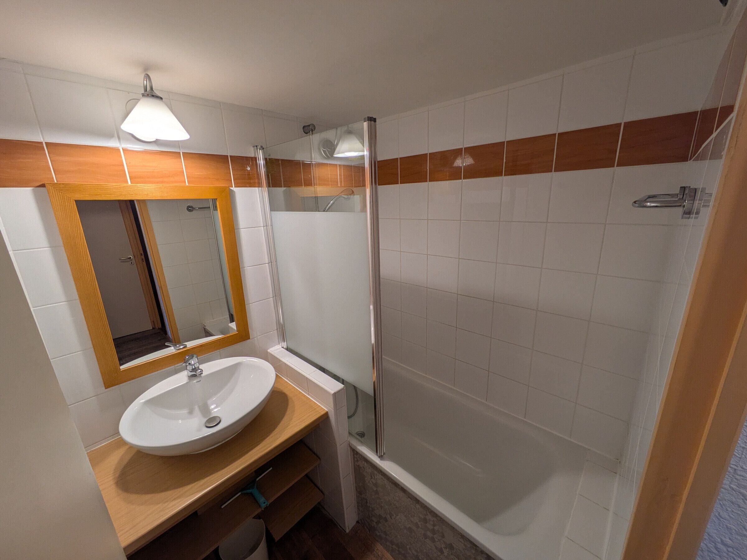 A bathroom with a sink, mirror, shower, and tiled walls.