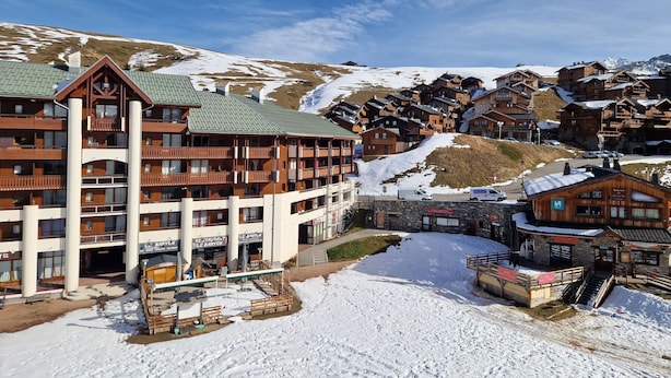 Et hotel med flere etager, en skilift, omgivet af snedækkede bjerge og klare himle.
