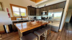 A modern kitchen with a large island, dark cabinets, stainless steel appliances, and a window providing natural light.