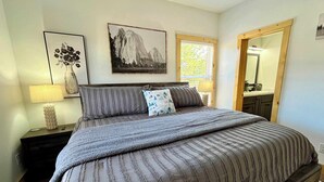 A bedroom with a bed, a nightstand, a lamp, a window, and a mirror.