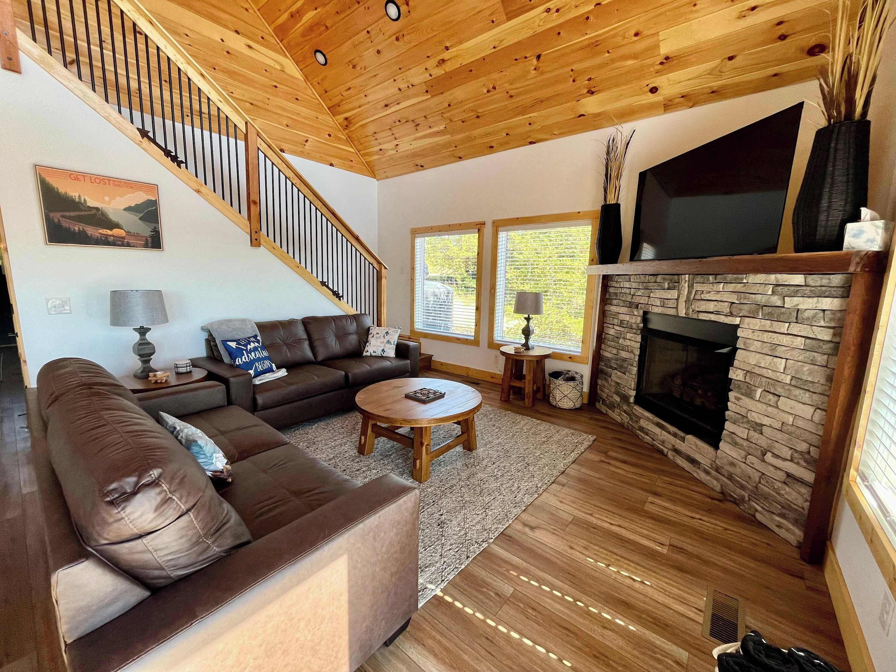 A living room with a brown leather sofa, a round wooden coffee table, a fireplace, and a staircase with wooden railings.
