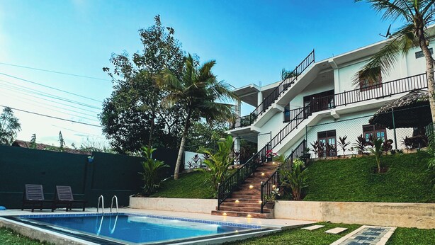 A modern house with a swimming pool, a staircase leading to a balcony, and a well-maintained lawn.