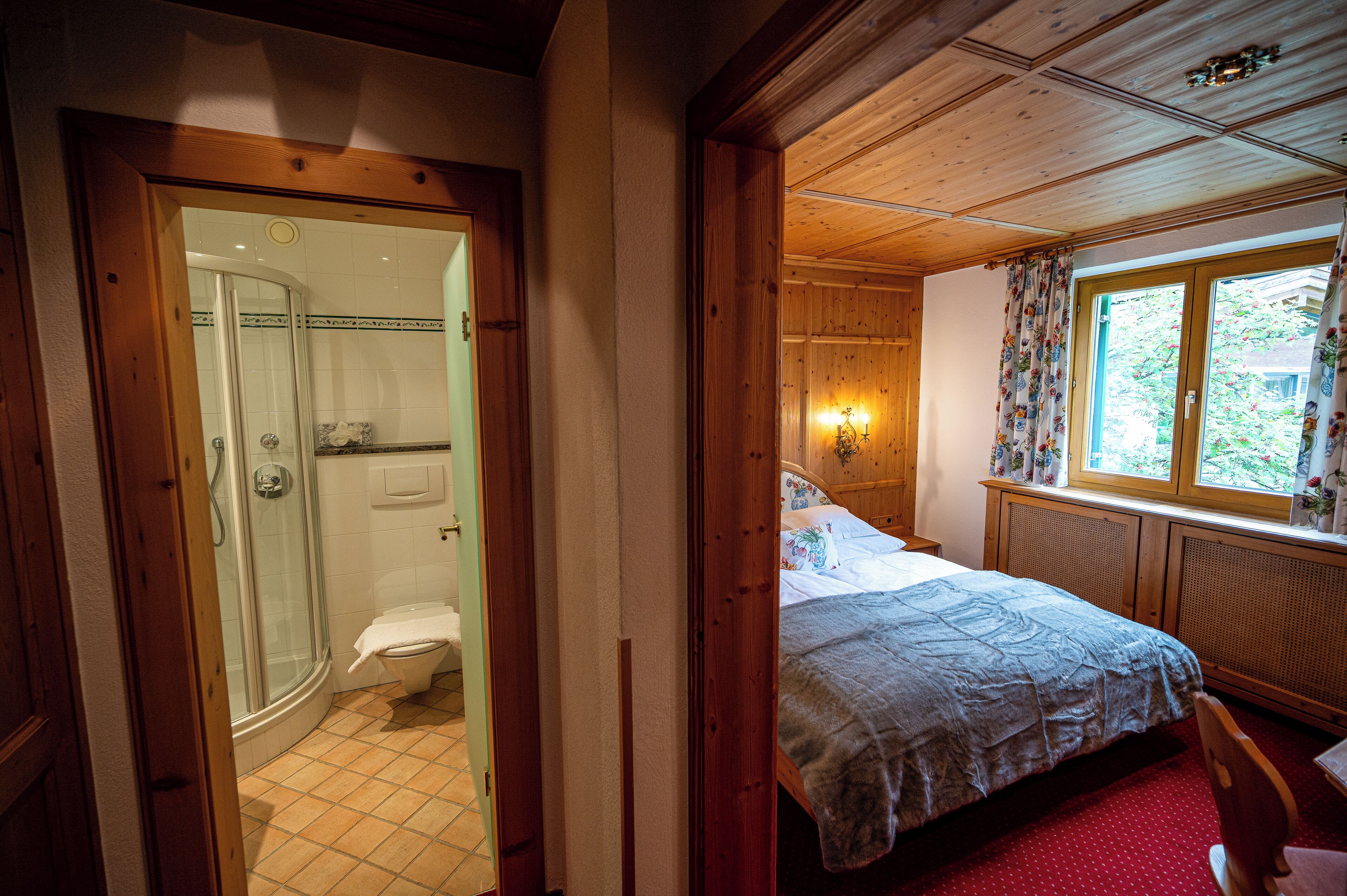 Un dormitorio con techo de madera, una ventana con cortinas florales y una cama con colcha estampada.
