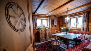 Interior de una cabaña de madera con una mesa de comedor, asientos tipo banco y una alfombra estampada.