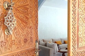 A room with a wooden door featuring intricate carvings, a grey sofa with cushions, and a small round table.