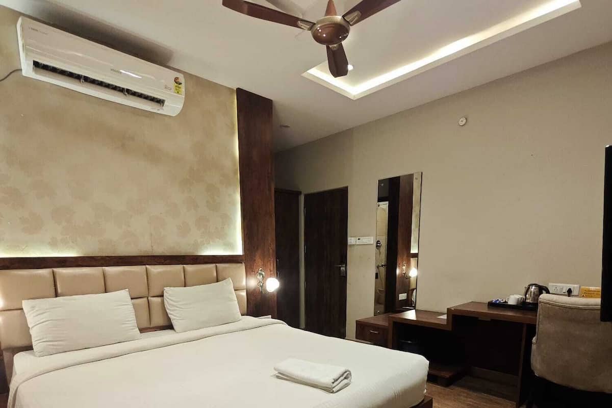Ein Hotelzimmer mit einem großen Bett, einem Deckenventilator, einer Klimaanlage, einem Schreibtisch mit Stuhl und einem Spiegel.