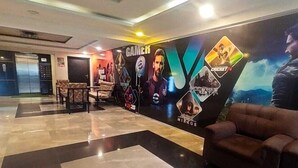 A lobby with a modern design, featuring a large wall mural with gaming and sports themes, a seating area with a brown sofa, and a tiled floor. - Stayz Royale Koramangala (Bengaluru)