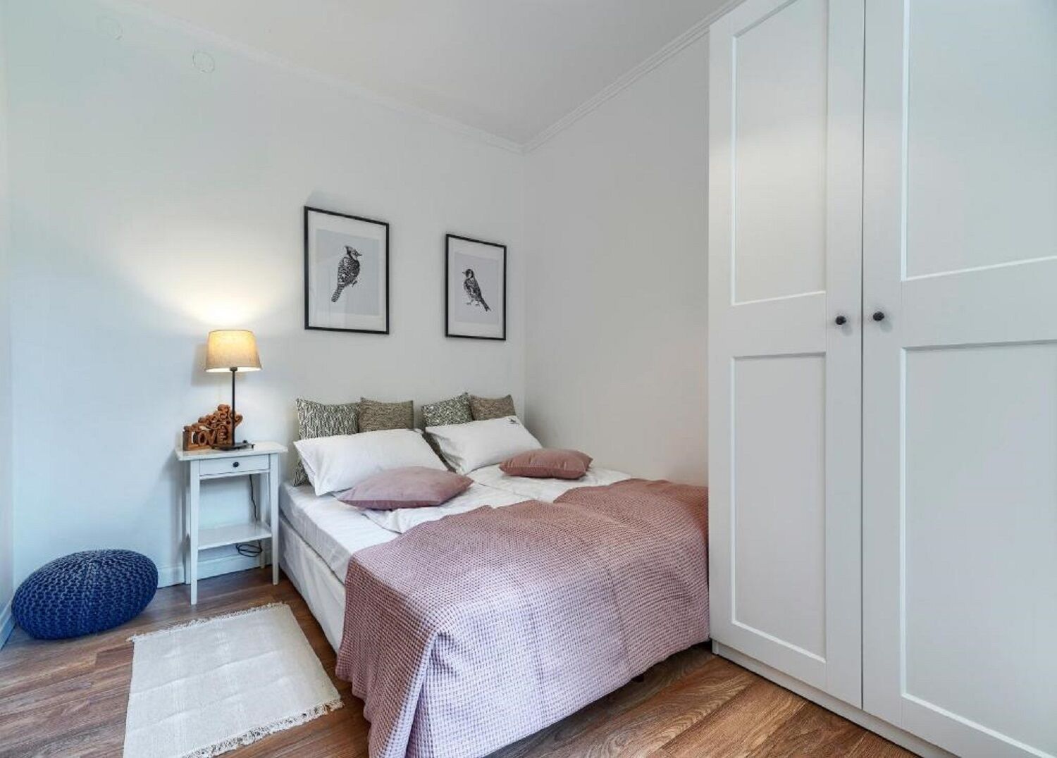 Une chambre à coucher avec un lit, une table de chevet, une lampe et deux tableaux encadrés accrochés au mur.