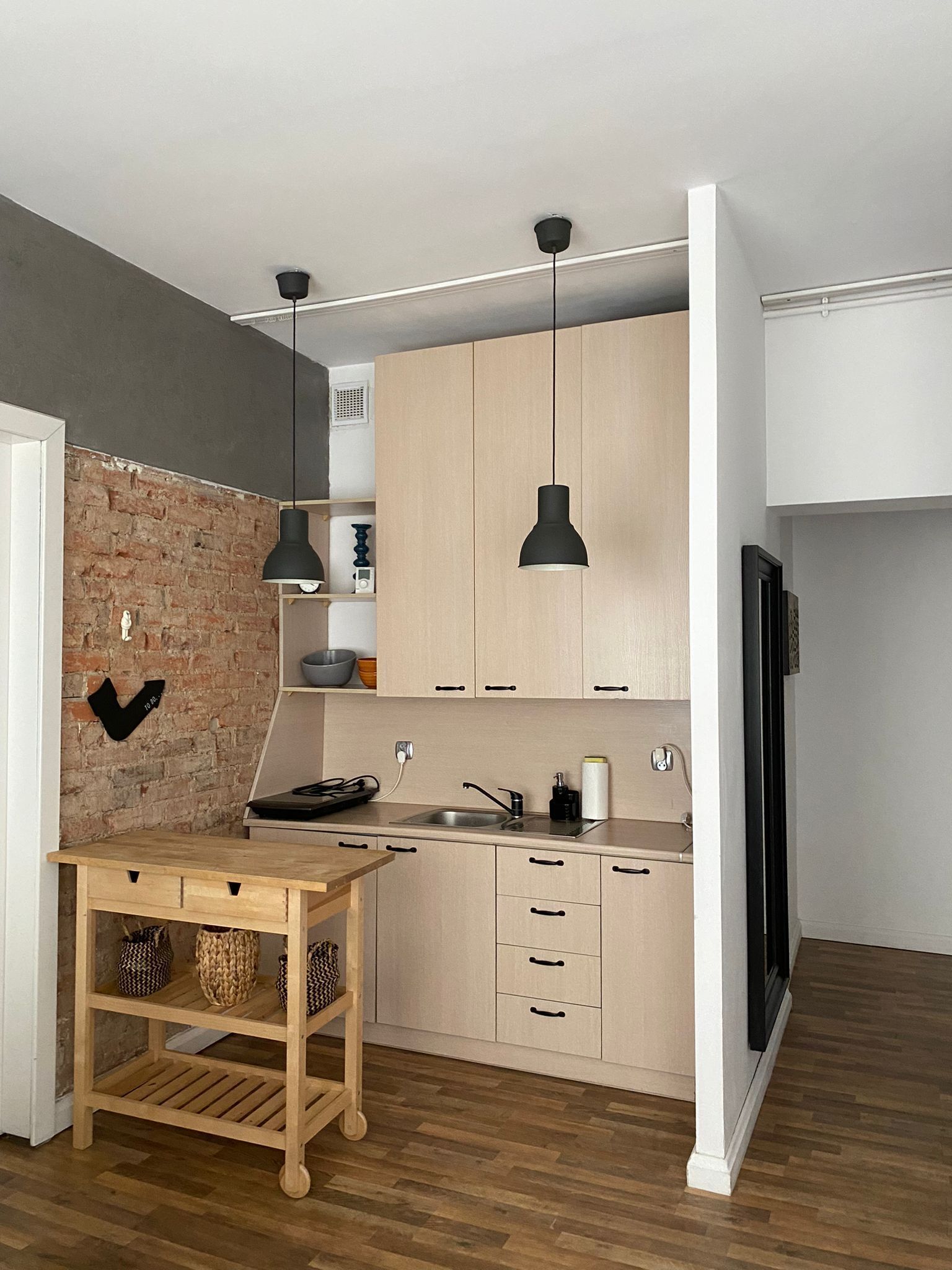 A modern kitchen with wooden cabinets, a brick accent wall, and pendant lighting.