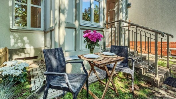 Un patio con dos sillas de mimbre, una mesa de madera y un jarrón con flores rosas.