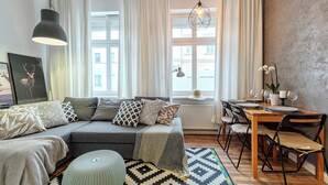 Una sala moderna con un sofá seccional, una mesa de comedor preparada para cuatro comensales y un ventanal con cortinas.