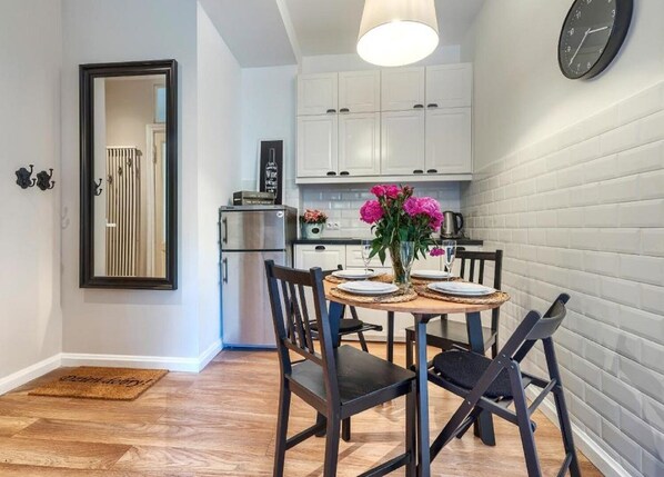 A modern kitchen with white cabinets, a stainless steel refrigerator, and a dining area with a round table set for four.