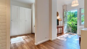 Un pasillo con suelo de madera, paredes blancas y una puerta que da a una habitación con vistas a zonas verdes.