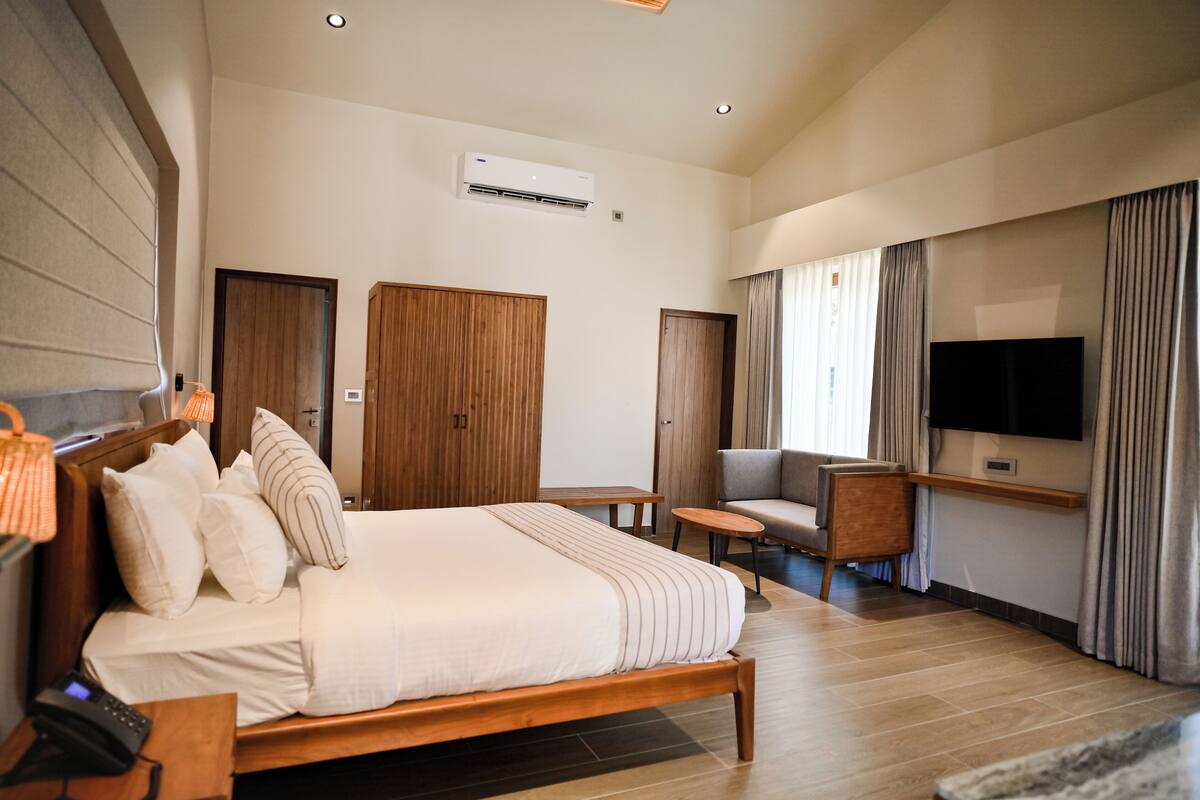 Una habitación de hotel moderna con una cama grande, televisión, sofá y armario de madera.