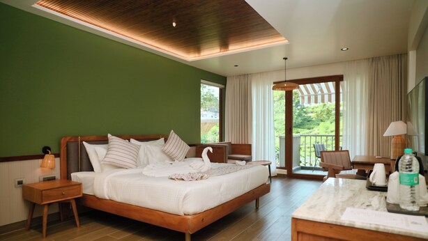 A hotel room with a large bed, a wooden nightstand, a desk with a chair, a large window, and a balcony.