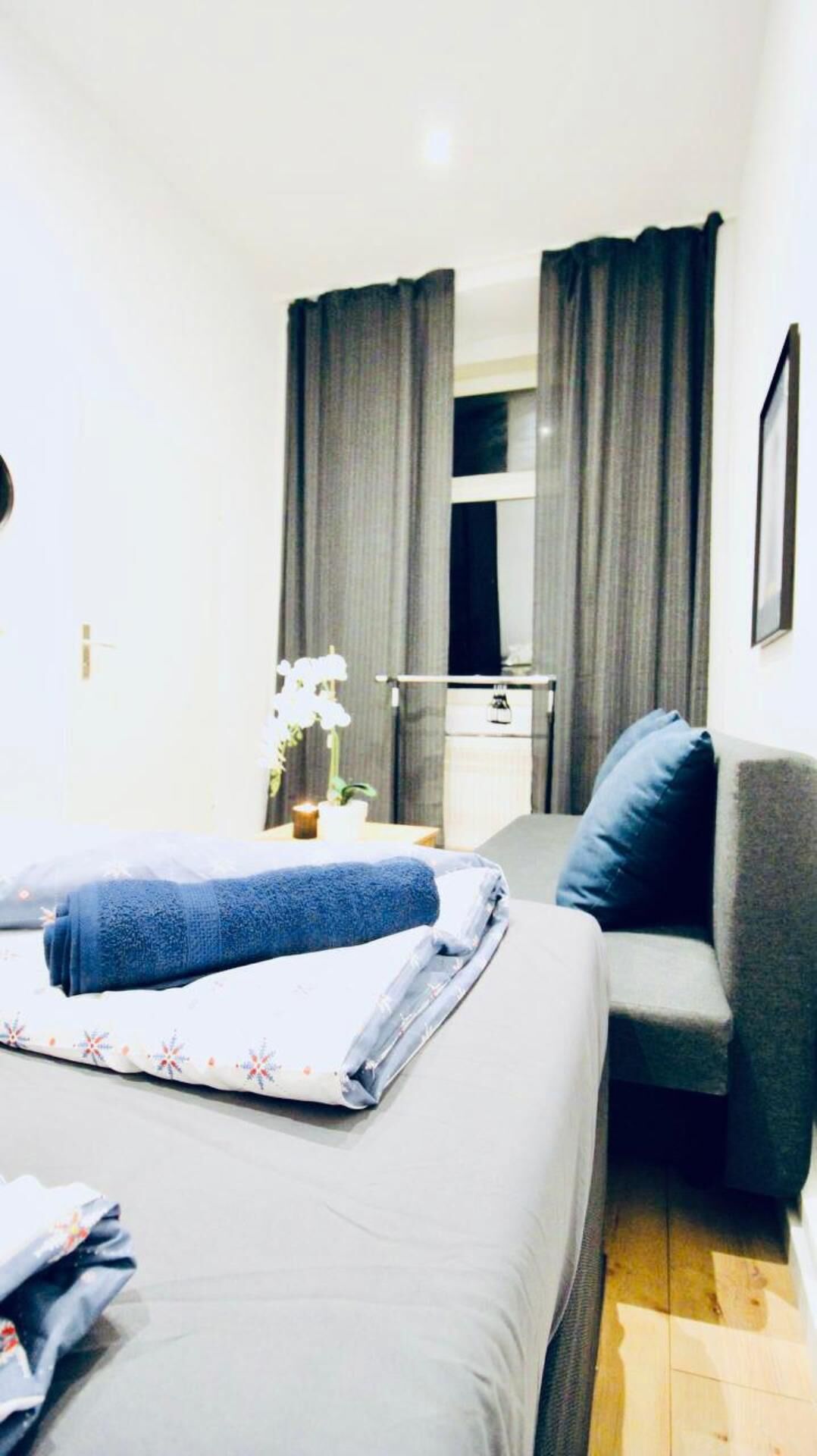 A hotel room with a bed, a sofa, a small table with a lamp, and a window with curtains.