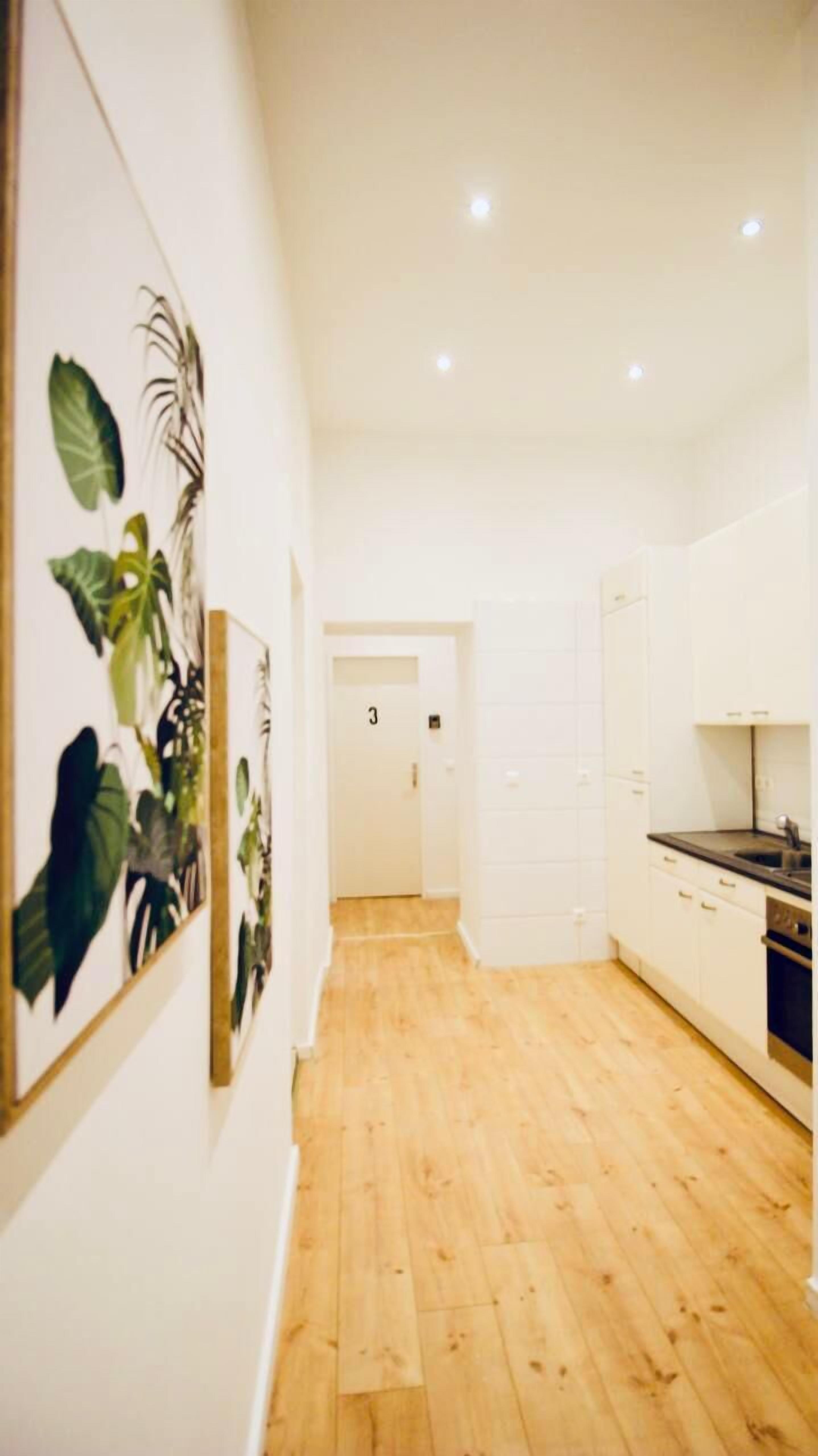 A modern kitchen with white cabinets, a wooden floor, and a door marked with the number 3.