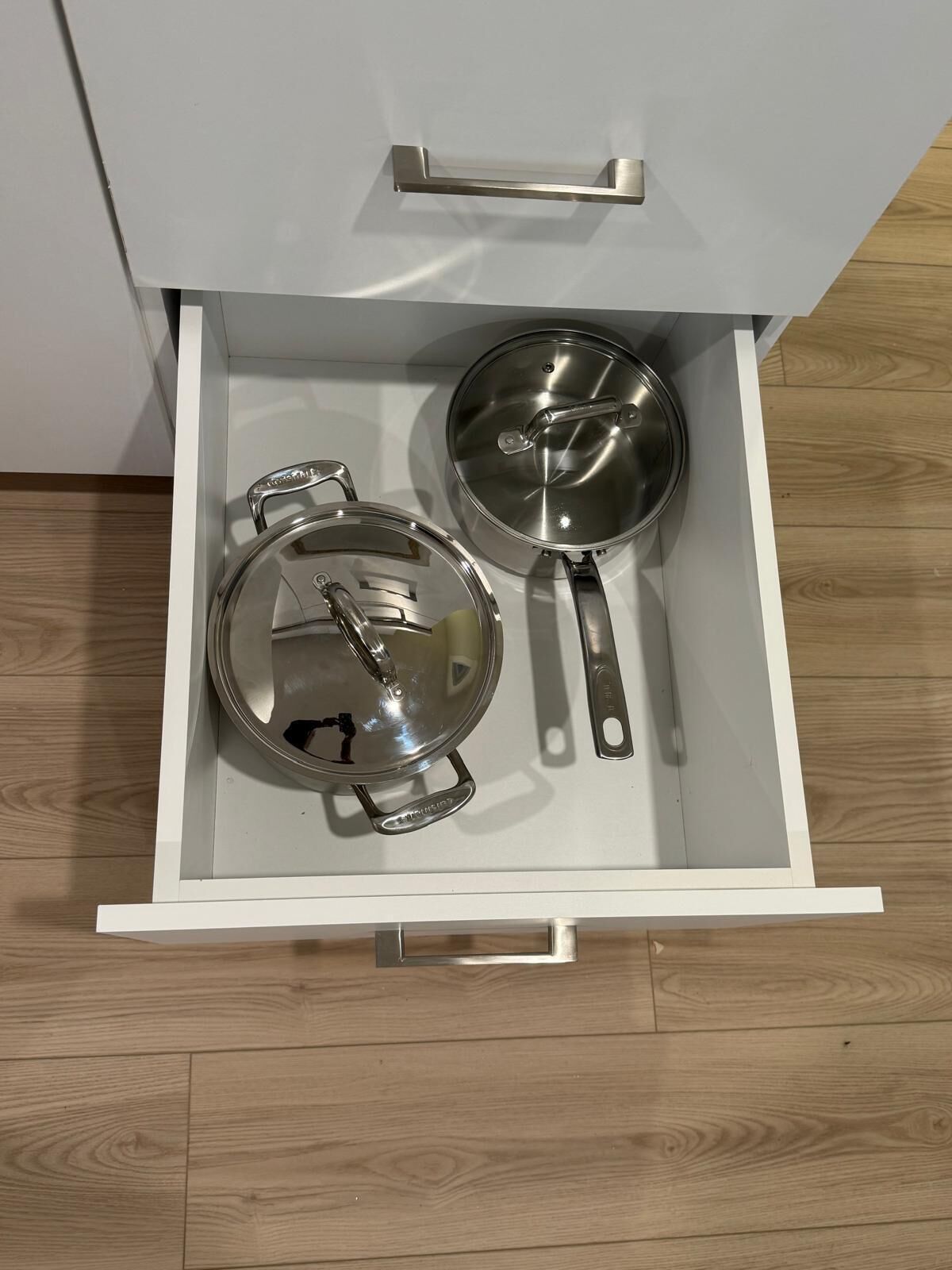 A drawer with two stainless steel pots and a pan.