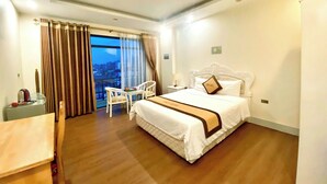 Habitación de hotel con una cama grande, una mesita, dos sillas, vista de la ciudad a través de un ventanal y un balcón.