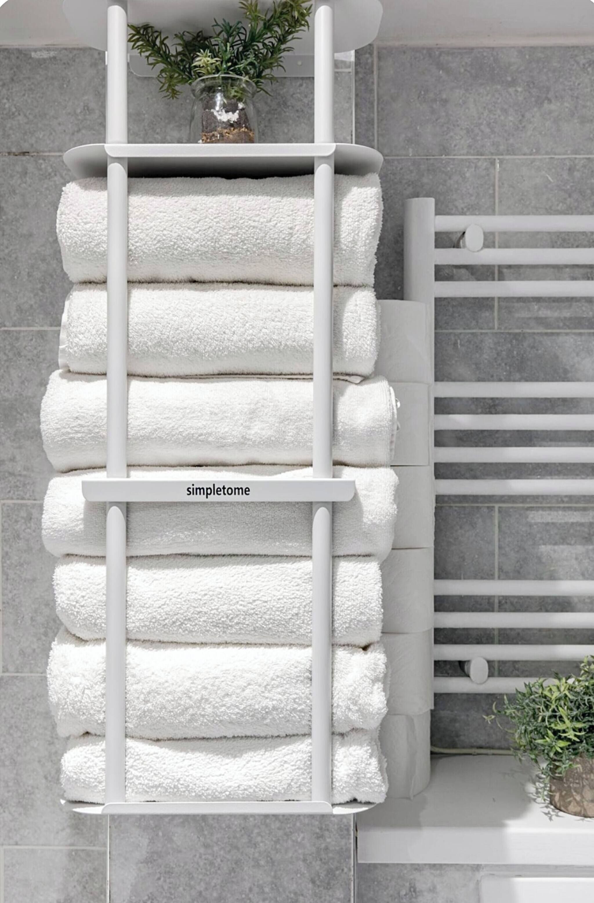 A white towel rack with multiple towels, a label reading 'simpletome,' and a potted plant on top.