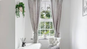 Une pièce au décor minimaliste, avec une chaise blanche, une petite table et une fenêtre avec des rideaux.
