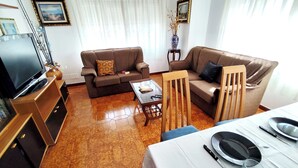 A living room with a sofa, coffee table, TV, and dining table set up. - Airtegal Litoral 49 (Cedeira)