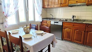 A kitchen with wooden cabinets, a dishwasher, and a dining table set for four. - Airtegal Litoral 49 (Cedeira)