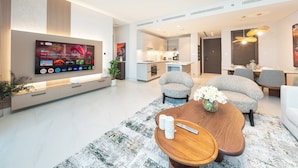 A modern living room with a flat-screen TV, comfortable seating, and a kitchen in the background. - PVH - Stunning 2BR - Creek Vistas Grande (Dubai)